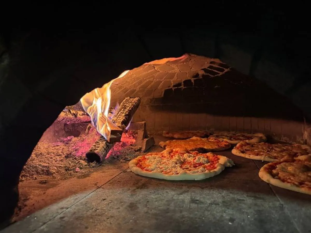 Il forno a legna acceso durante il servizio, con le pizze in cottura